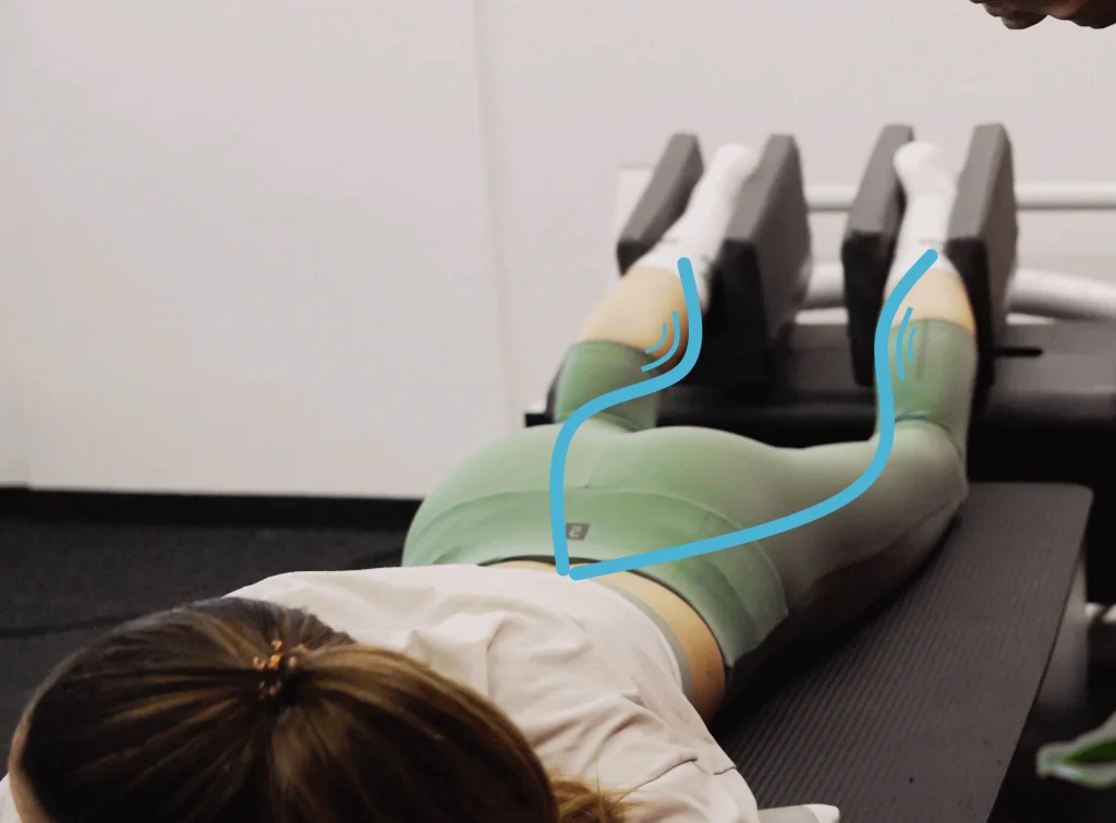 Personne en position d'entraînement, les jambes maintenues dans un dispositif spécialisé doté de la technologie Kinetic Wave, représentant une innovation dans le domaine de la santé et des performances sportives.